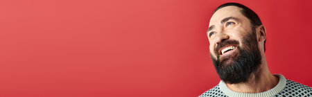 happy bearded man in winter sweater with ornament smiling on red backdrop, Merry Christmas bannerの写真素材