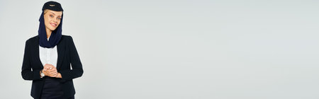 charming stewardess in headscarf and elegant uniform of arabian airlines standing on grey, bannerの写真素材