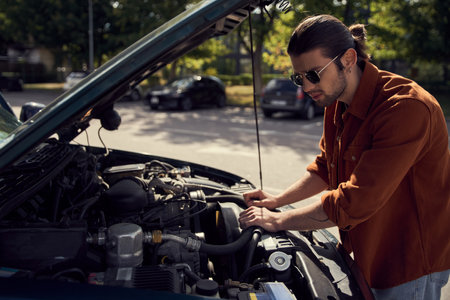 attractive stylish male model in trendy urban attire with accessories checking on his car engineの写真素材