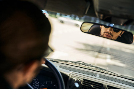handsome sexy male model with sunglasses behind steering wheel and looking in rearview mirrorの写真素材
