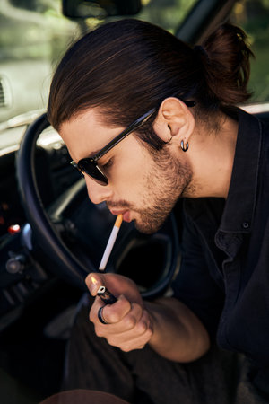 handsome sexy male model with earring and sunglasses lighting up his cigarette in car, sexy driverの写真素材