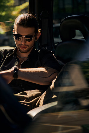 vertical shot of good looking appealing man with tattoo relaxing on backseat of his car, sexy driver