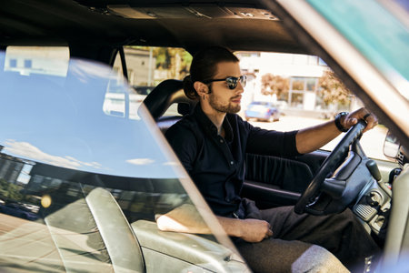 handsome young man with accessories in black shirt sitting behind steering wheel, sexy driverの写真素材
