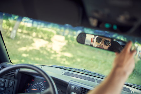 appealing man with stylish sunglasses looking at his rearview mirror, fashion and styleの写真素材