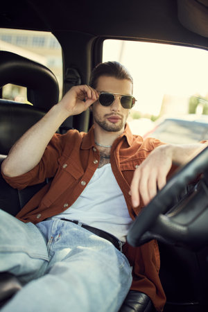 good looking young man in stylish outfit touching his sunglasses while relaxing in car, sexy driverの写真素材