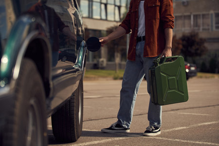 cropped view of young trendy man in brown stylish shirt with jeans refueling his car with petrol