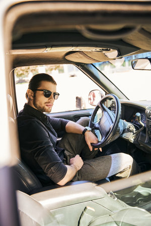 vertical shot of good looking sexy male model in stylish attire looking at camera at steering wheelの写真素材