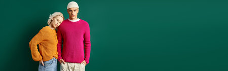 stylish couple in fashionable outfits posing with hands in pockets on turquoise background, bannerの写真素材