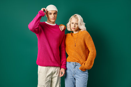 fashionable man and blonde woman in winter outfits posing together on turquoise background