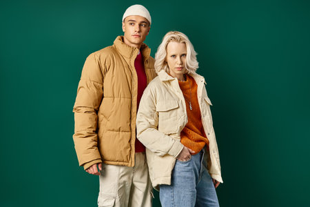 young man and woman in puffer jackets posing together on turquoise background, stylish couple