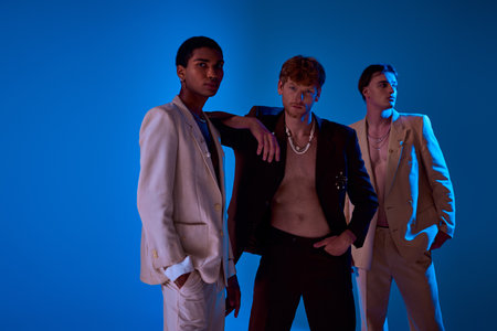 handsome diverse men posing actively in elegant suits with accessories on blue backdrop, fashionの写真素材