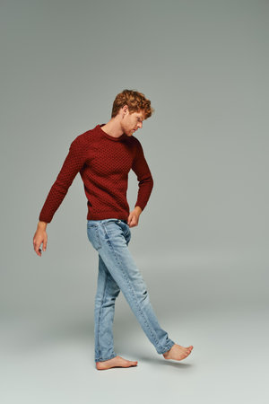 handsome appealing bearded man in warm sweater walking barefoot on gray backdrop, fashion conceptの写真素材