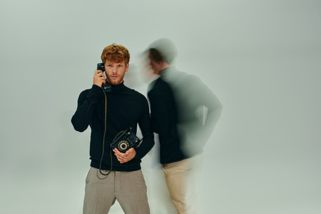 red haired man in elegant turtleneck with landline phone with other man moving, long exposureの写真素材