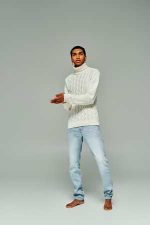 good looking african american man in white sweater with accessories posing on gray backdrop, fashionの写真素材
