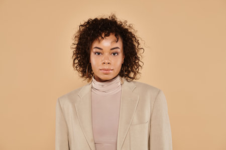 beautiful african american woman with curly hair posing in autumnal blazer on beige backdrop, bannerの写真素材