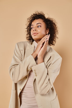 autumn trends, brunette african american woman posing in turtleneck and blazer on beige backdropの写真素材