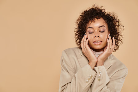 autumn fashion, african american woman with closed eyes posing in blazer on beige backgroundの写真素材