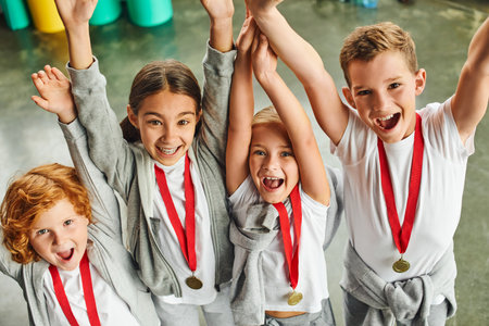 happy little boys and girls in sportswear with golden medals cheering and smiling at camera