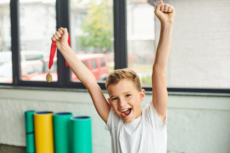 joyful preadolescent boy cheering and holding golden metal, smiling happily at camera, child sportの写真素材