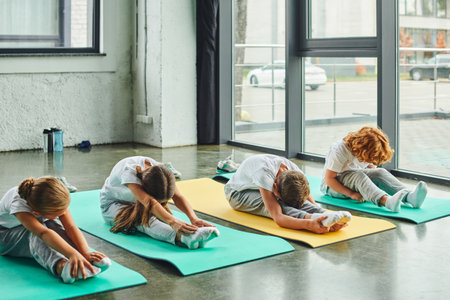 preadolescent cute boys and girls sitting on fitness mats and stretching actively, child sportの写真素材