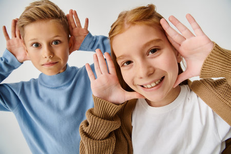 joyous little friends in casual attires smiling at camera with hands near faces, fashion conceptの写真素材