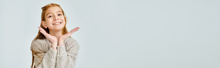 pretty little girl in casual sweater looking at camera, hands under face, fashion concept, bannerの写真素材