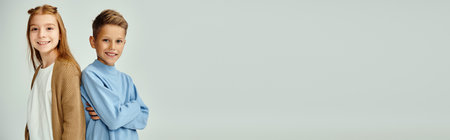 jolly little friends in warm attires posing back to back looking at camera, fashion concept, bannerの写真素材