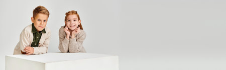 happy little friends next to white cube smiling at camera, hands under chin, fashion concept, bannerの写真素材