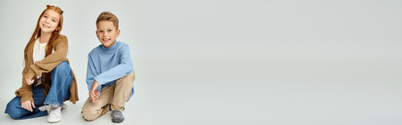 little friends in winter casual clothes squatting and smiling at camera, fashion concept, bannerの写真素材