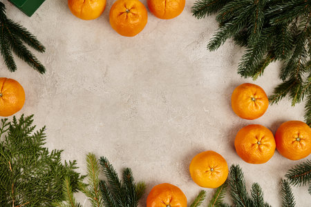 Christmas frame with sweet tangerines near juniper and pine branches on grey textured surface