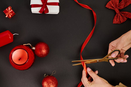 cropped view of woman cutting ribbon with scissors near baubles and Christmas decor on blackの写真素材