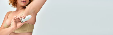 cropped view of curvy woman in lingerie applying roll-on deodorant on armpit, horizontal banner