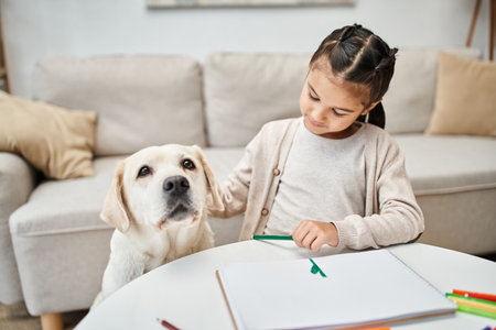 little girl in casual clothes drawing with color pencil and cuddling labrador in living room, artの写真素材
