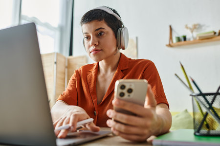 attractive young student studying at her laptop with mobile phone and pen in hands, educationの写真素材