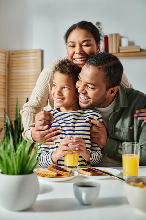 vertical shot of cheerful african american family hugging warmly each other at breakfast tableの写真素材