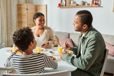 happy african american family in casual attires smiling lovingly at each other during breakfastの写真素材