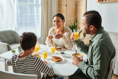 cheerful modern african american family having breakfast together and smiling at each otherの写真素材