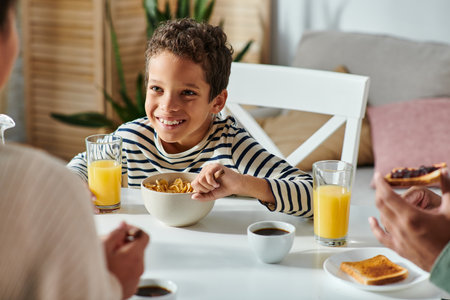 african american parents having breakfast together with their cheerful little son eating corn flakesの写真素材