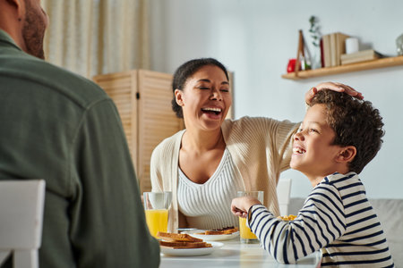 cropped view of african american man sitting at breakfast table in front of his jolly wife and sonの写真素材