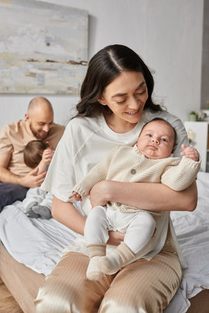 vertical shot of mother holding her newborn baby with her blurred husband and little son on backdrop