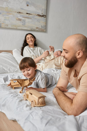 vertical shot of father playing with his little son with blurred wife and newborn baby on backdrop