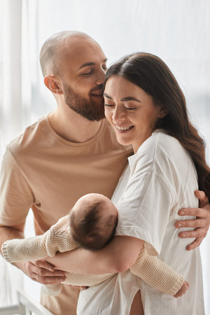 vertical shot of jolly happy parents hugging lovingly and holding their newborn baby boy, family