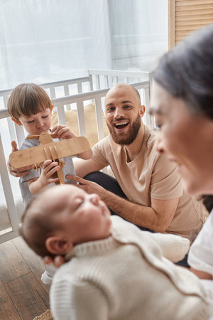 focus on bearded father playing with his son and looking at his blurred wife holding their baby boy