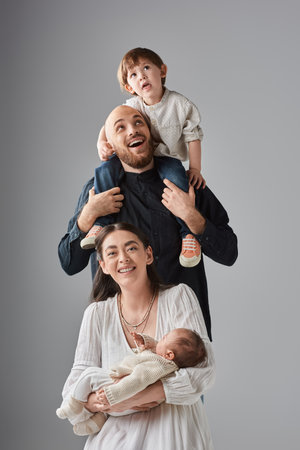 cheerful mother sitting with baby with her husband holding their little son on shoulders behind her