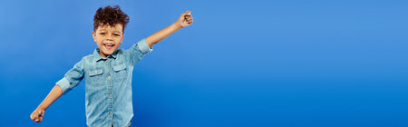 portrait of excited african american boy in denim attire looking at camera on blue backdrop, bannerの写真素材