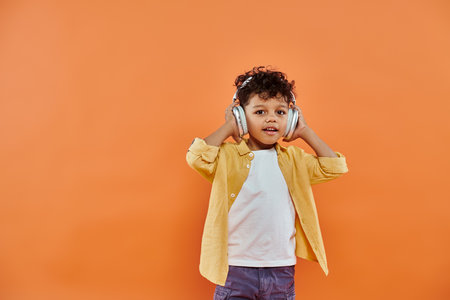 happy and curly african american boy listening music in wireless headphones on orange backgroundの写真素材