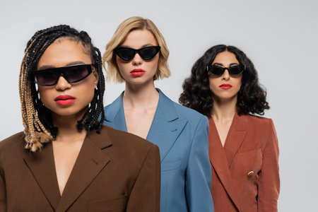 group portrait of trendy multiracial girlfriends in dark sunglasses and colorful suits on greyの写真素材