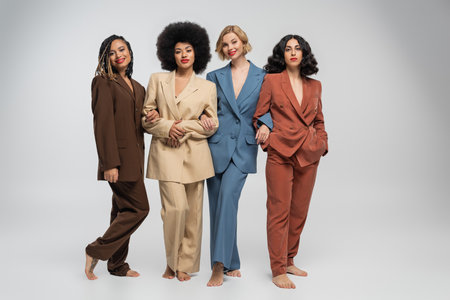 multicultural barefoot female models standing in colorful suits on grey backdrop, full lengthの写真素材
