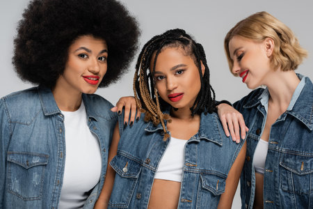diverse and charming multiracial girlfriends in blue denim attire posing on grey, modern fashionの写真素材