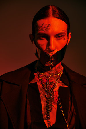vertical shot of young stylish man in futuristic laced mask with tattoos on face, fashion concept